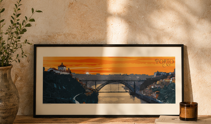 A framed art print of a sunset over Porto, Portugal, leaning against a textured beige wall on a wooden surface next to a plant and a candle.