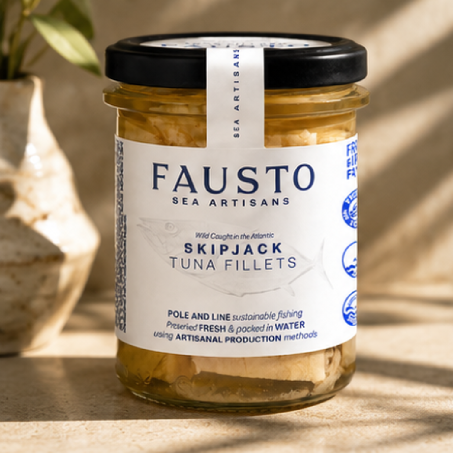 A jar of Fausto Sea Artisans Skipjack Tuna Fillets on a stone surface with warm natural light and shadows, next to a garlic bulb.