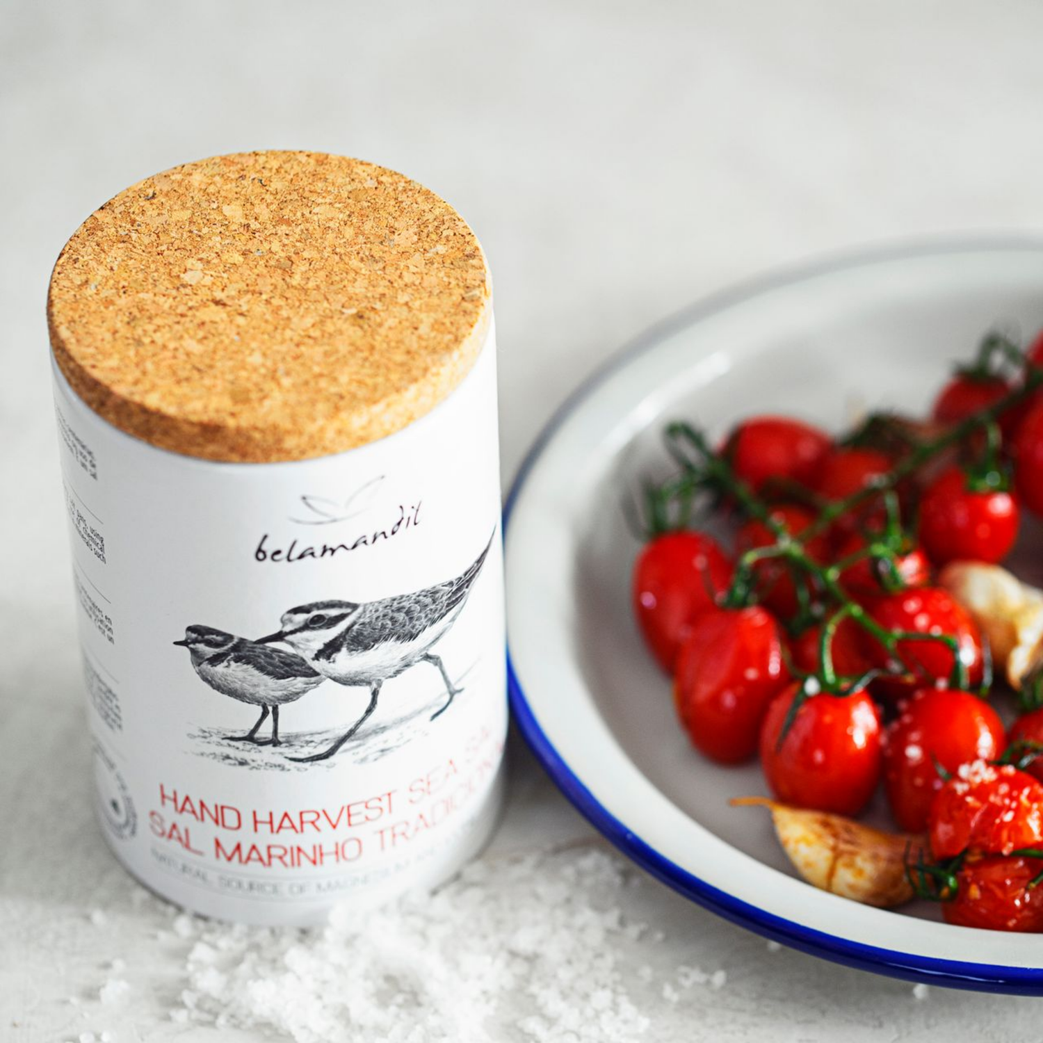 Jar of Belamantil sea salt with a cork lid next to a plate of tomatoes and garlic.