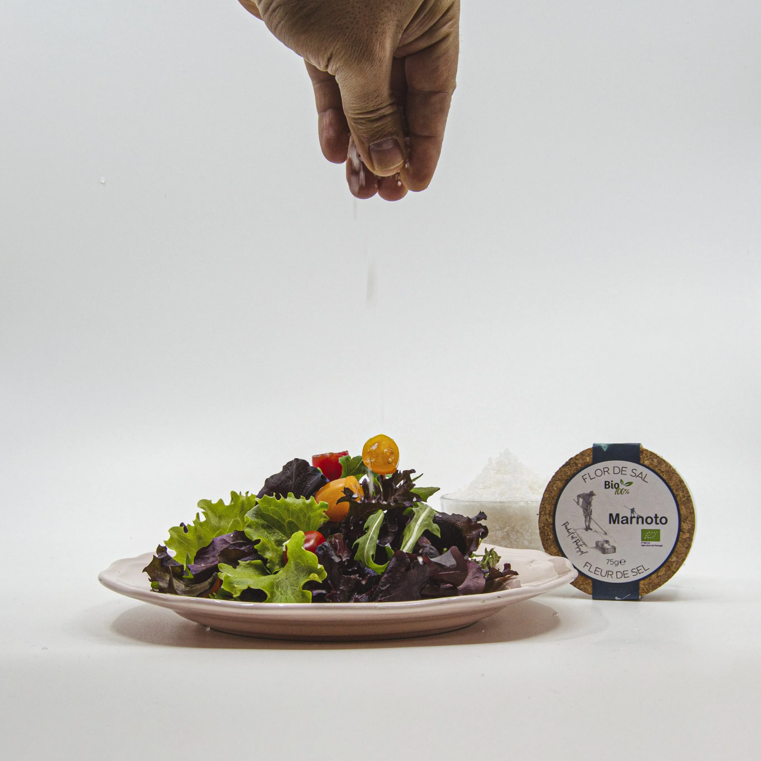 Hand reaching towards a plate of salad with a Marnoto product on a white background