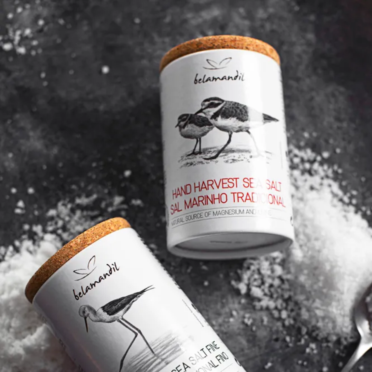 Two containers of belamandii sea salt with bird illustrations on a dark background.