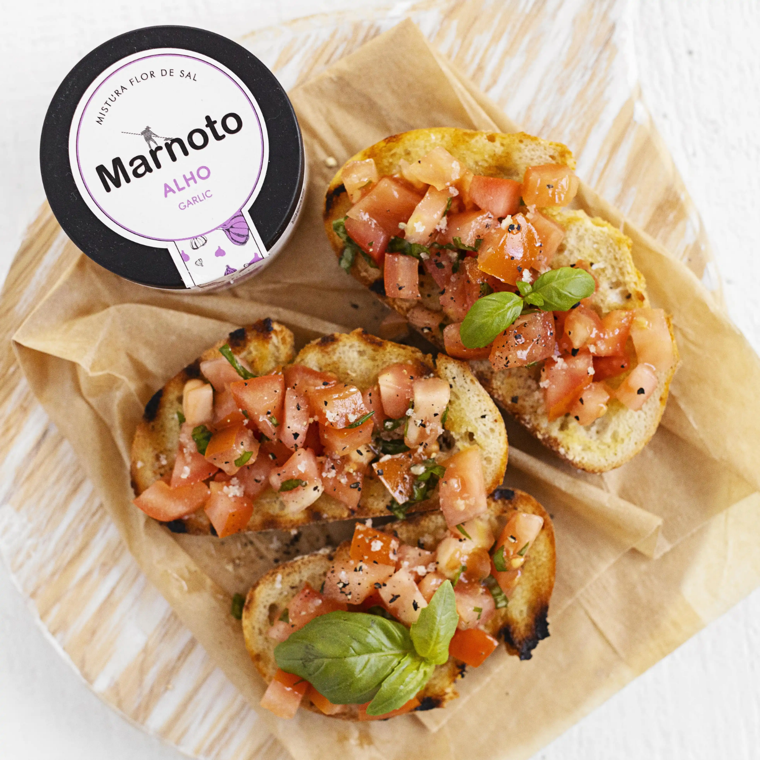 Bruschetta with tomatoes and basil on a piece of paper, next to a container labeled 'Marnoto'.