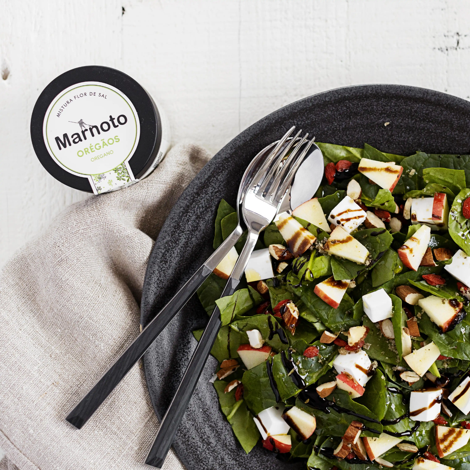 Salad with apples and nuts on a dark plate with Marnoto oregano packaging.