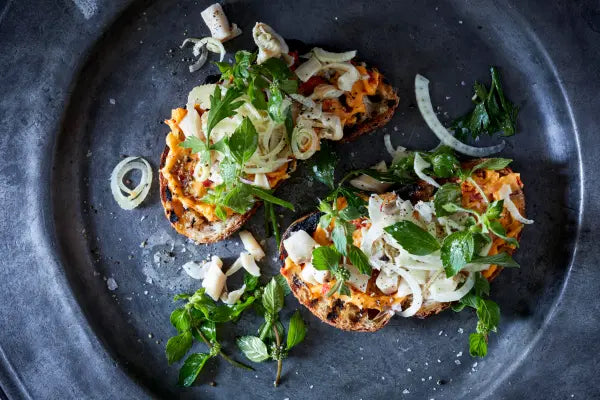 Plated dish with toasted bread topped with vegetables on a dark surface