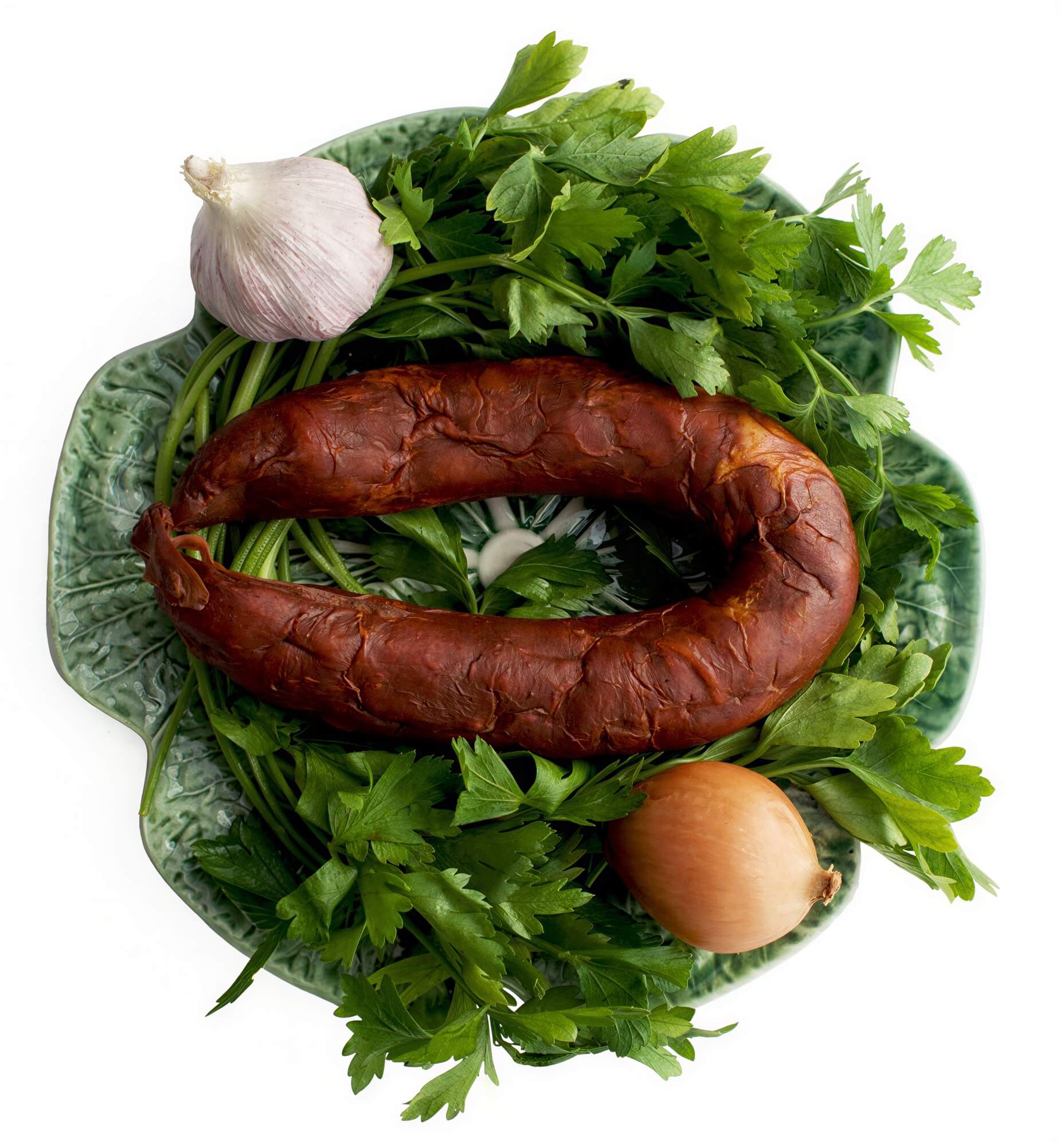 A traditional Portuguese sausage, Chouriço Caseiro, displayed on a plate with parsley, garlic, and an onion.