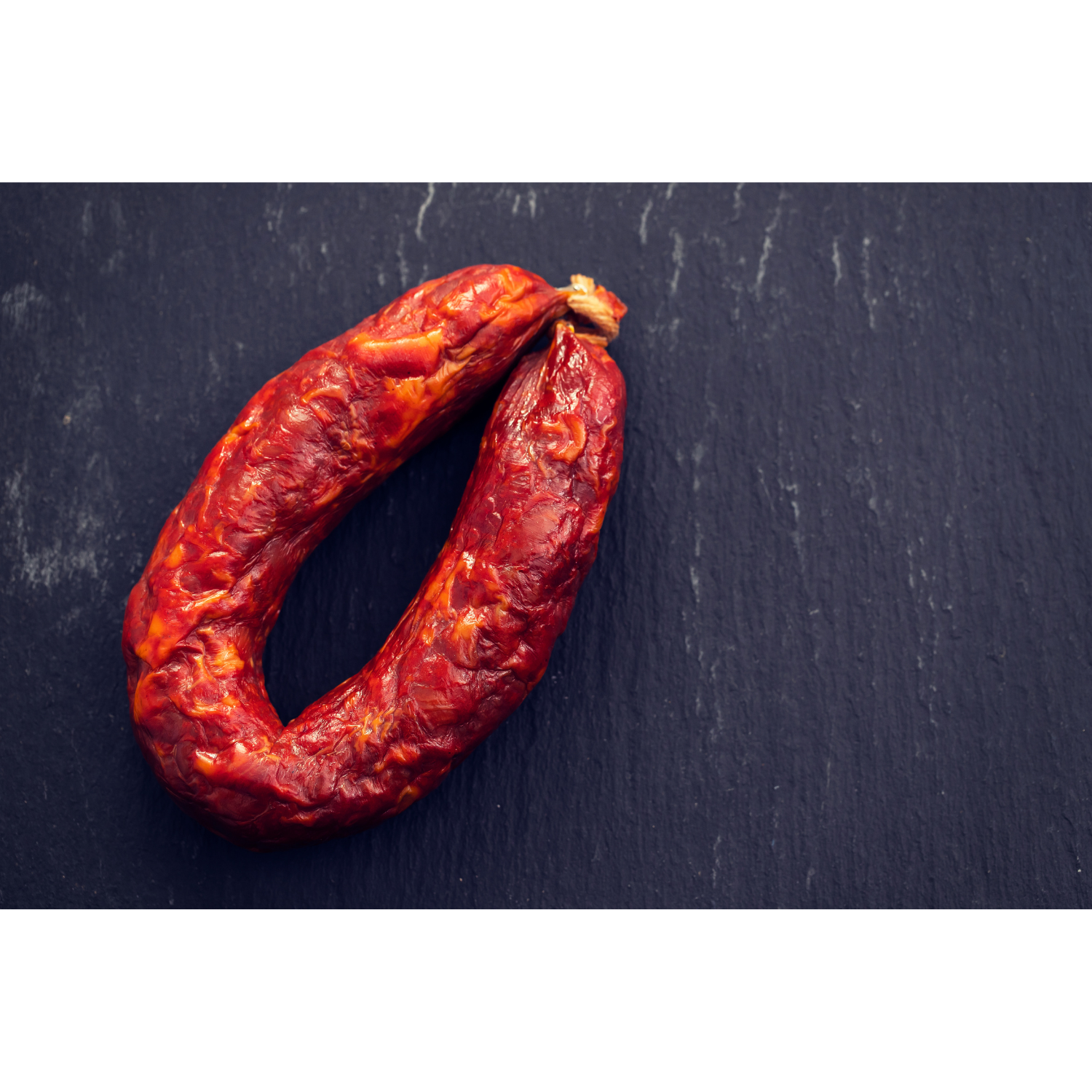 Chouriço caseiro, a red, cured sausage, displayed on a dark slate surface.