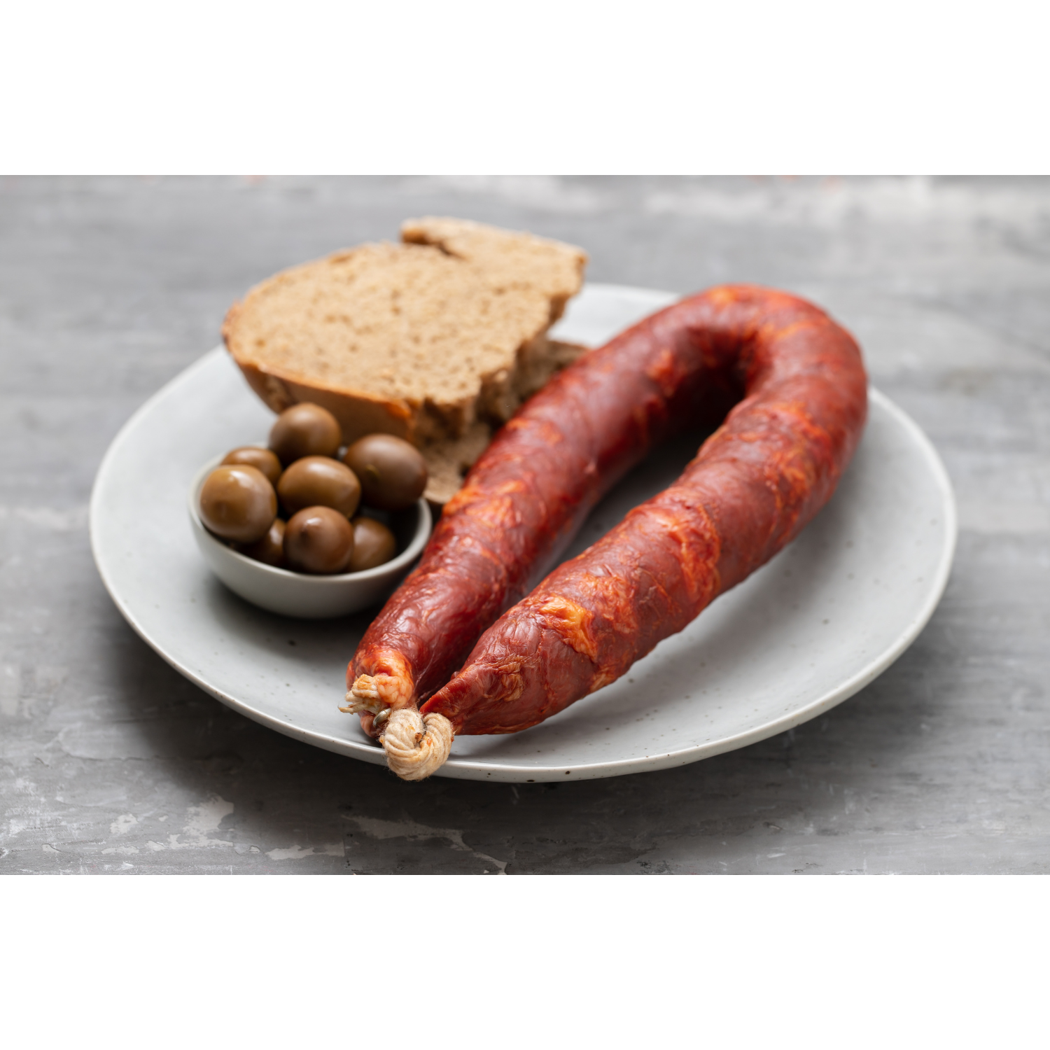 Chouriço caseiro sausage on a plate with olives and brown bread slices.