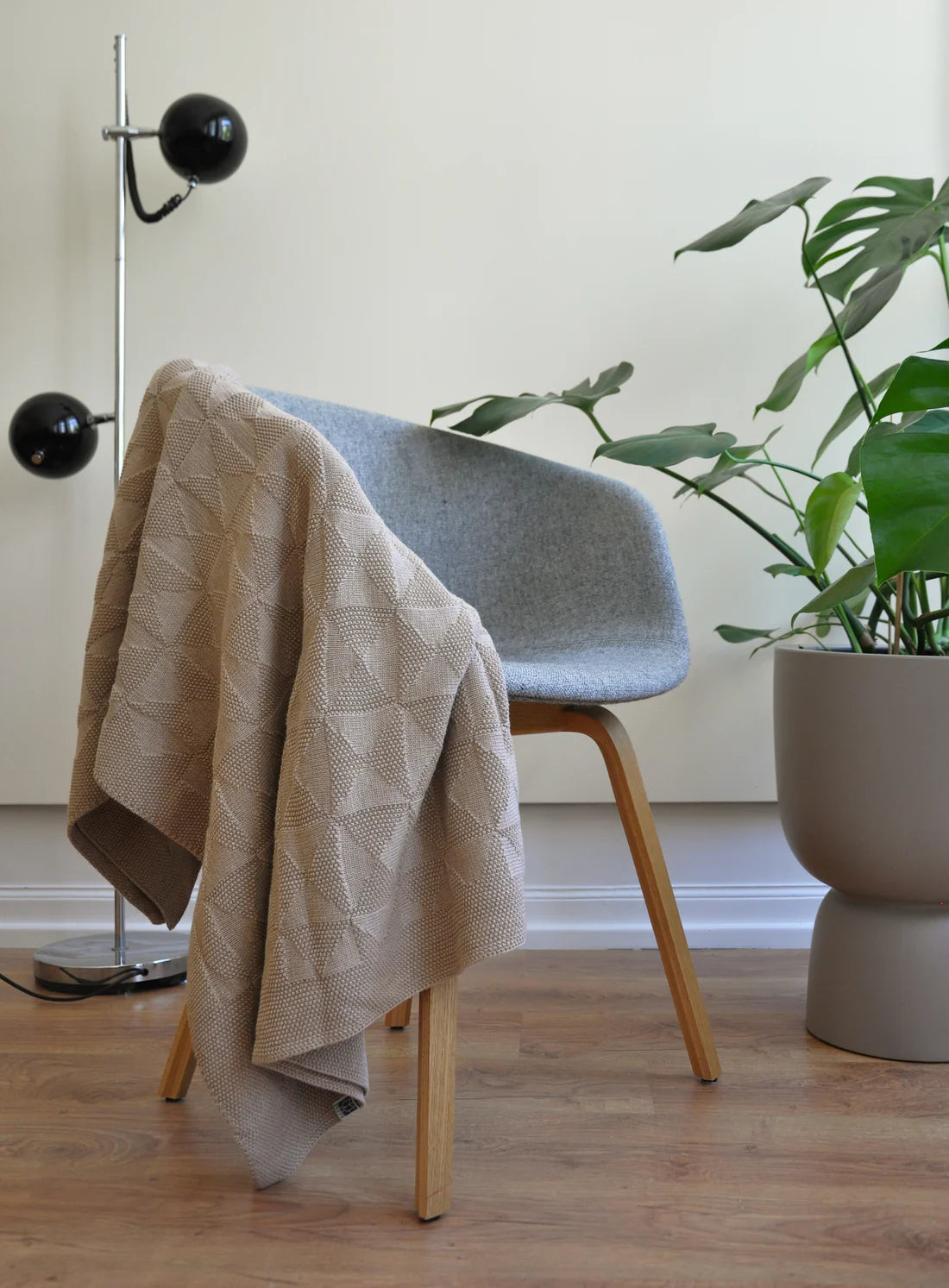 Blue chair with a beige blanket draped over it, next to a plant in a room with wooden flooring.