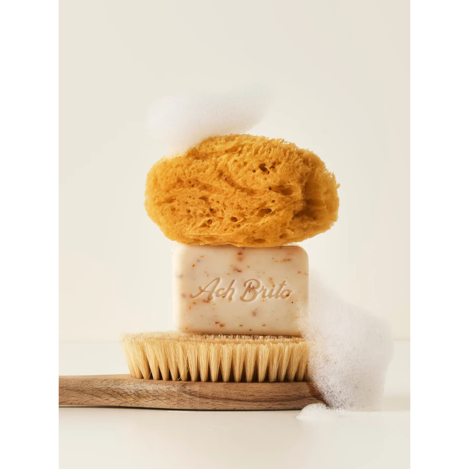 Bar of soap with a natural sponge and brush on a wooden block against a white background