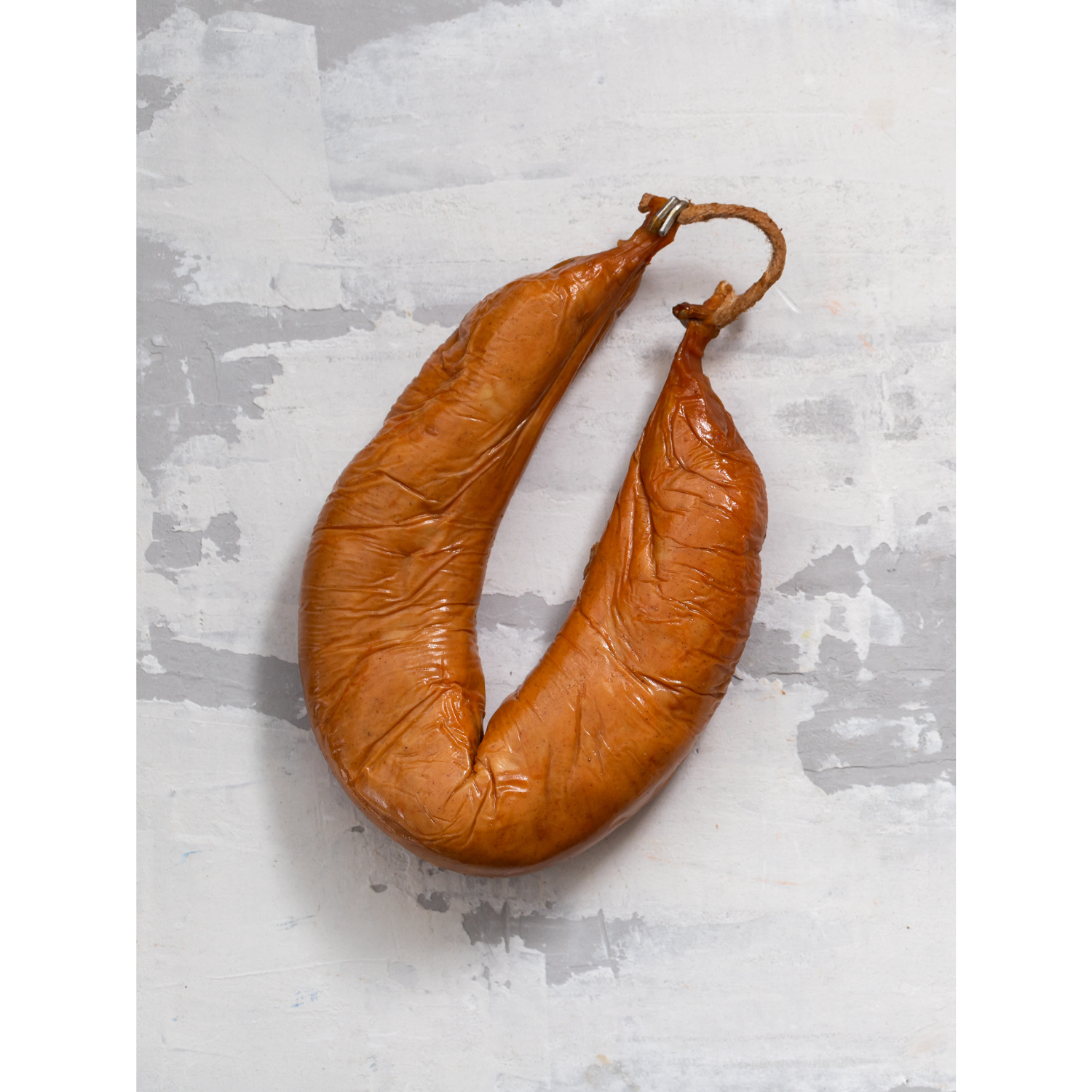 Farinheira sausage in a curved shape, with a brown, glossy exterior and a tied end, displayed on a light textured background.