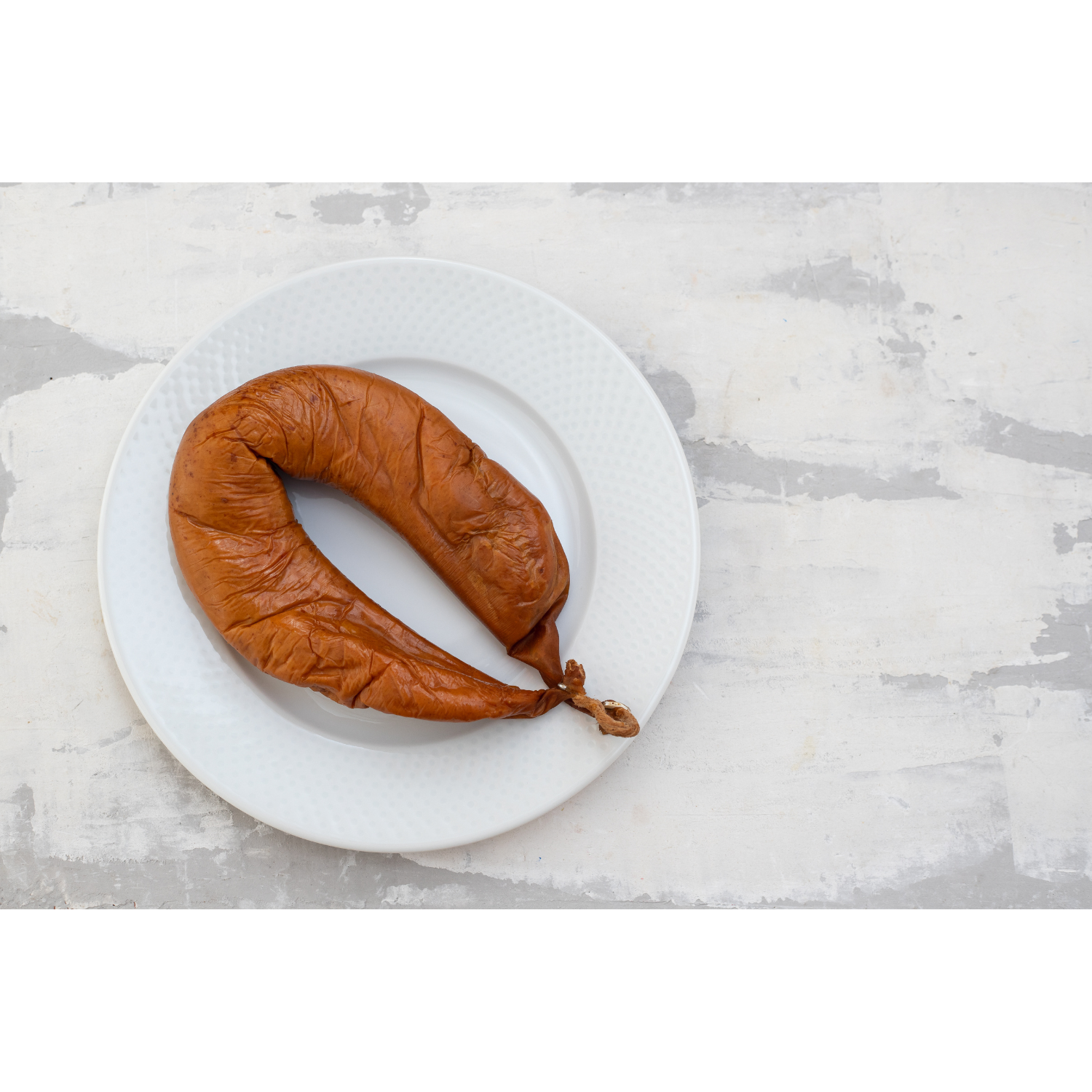 Farinheira sausage on a white plate, featuring a brown, curved shape against a light textured background.