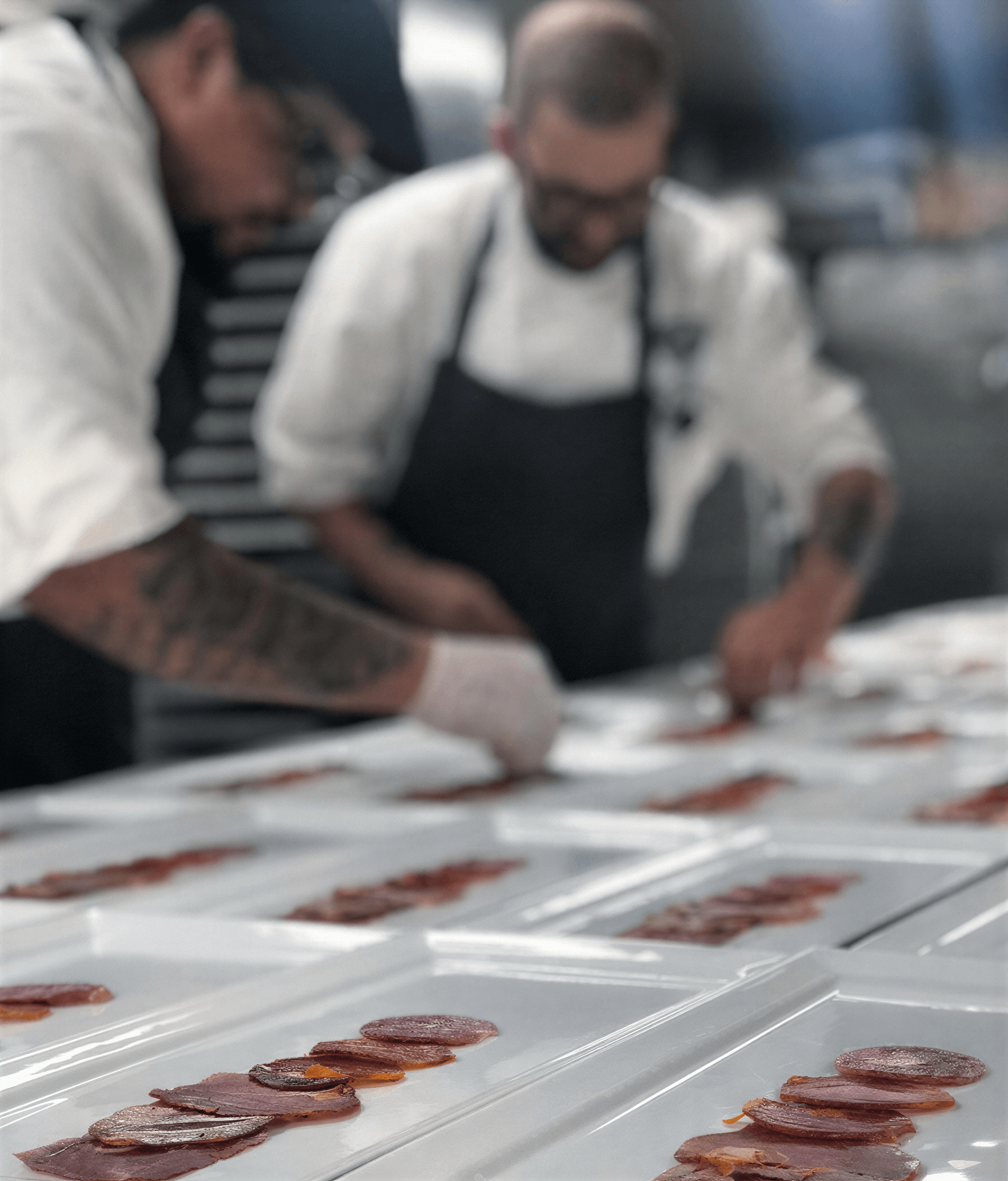 Two chefs arranging slices of Fermin Iberico chorizo on white plates in a kitchen setting.