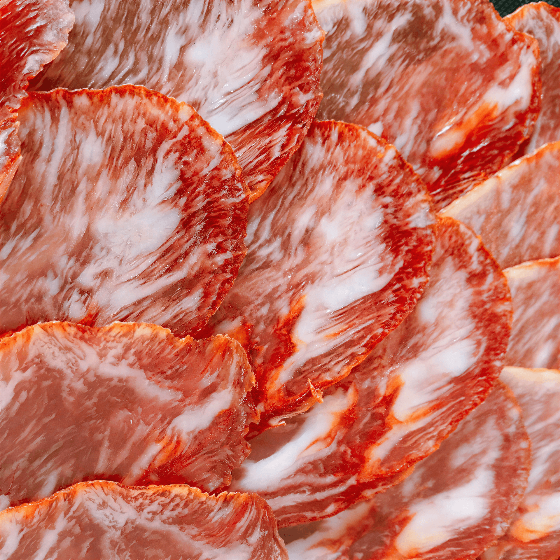 Fermin 100% Iberico acorn-fed loin, thinly sliced with marbled fat and a reddish hue, arranged in a circular pattern.