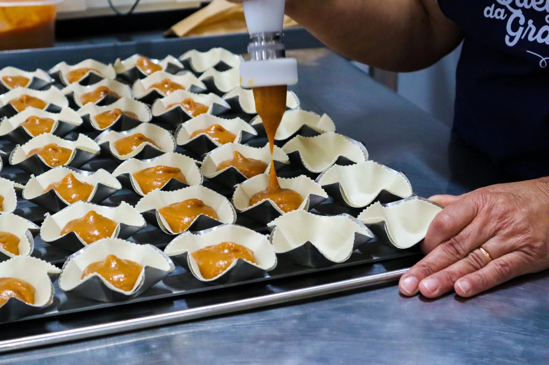 Queijadas da Graciosa being poured into molds on a baking tray, with a hand holding the nozzle.