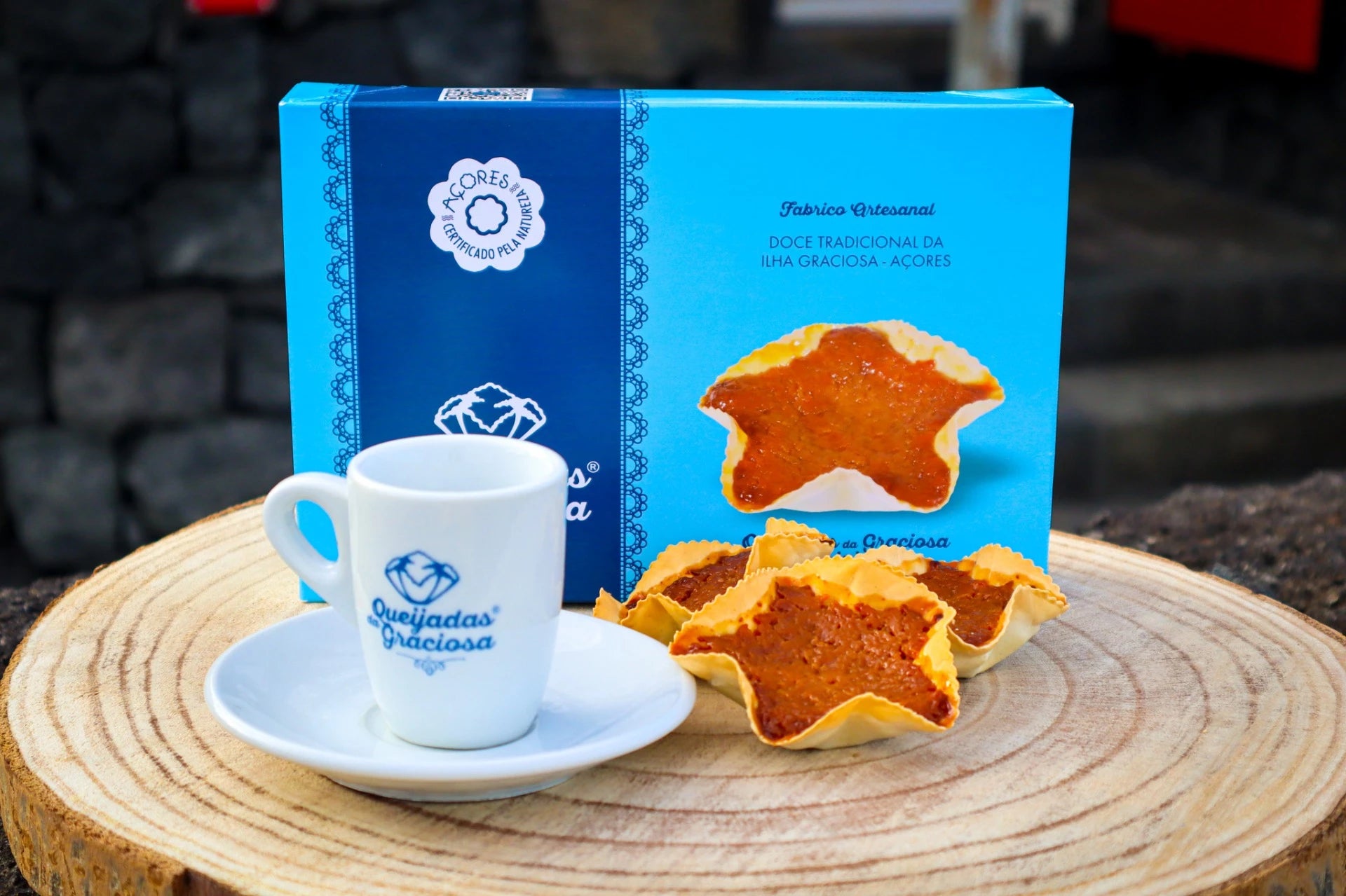 Queijadas da Graciosa box with traditional pastries, a small cup, and wooden serving board.