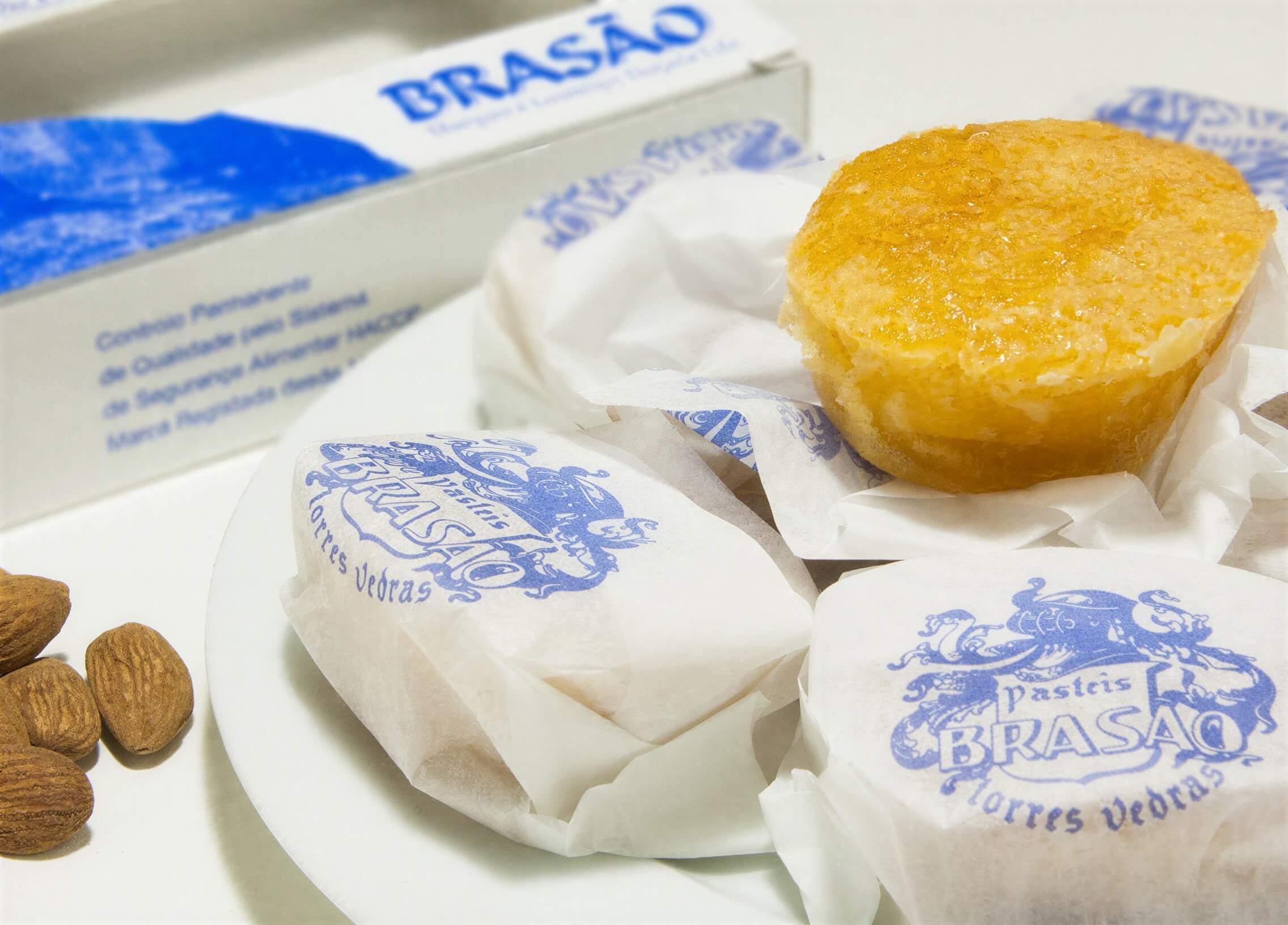 An unwrapped Brasao Bean Pastry on top of wrapped Bean Pastries (Pasteis de Feijao) with almonds on the side